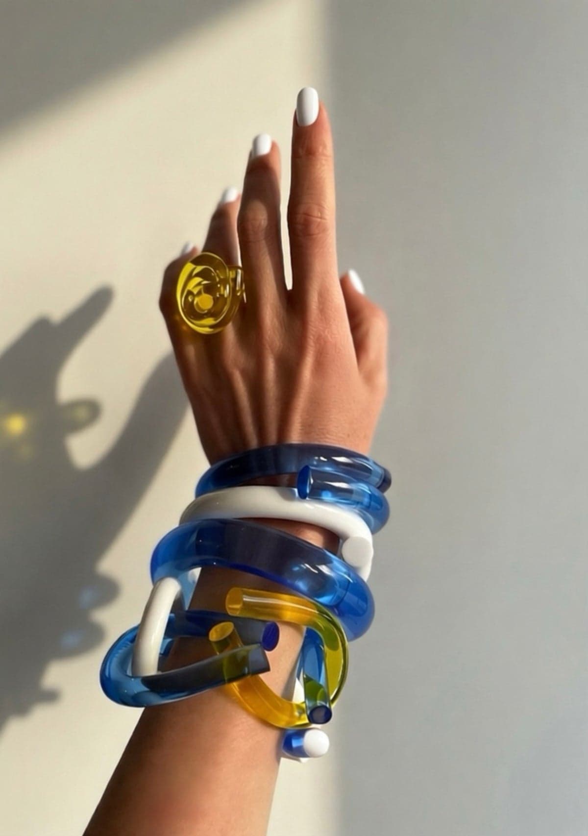 Chofa Jewelry yellow lucite ring and blue lucite bangles worn on a hand in sunlight